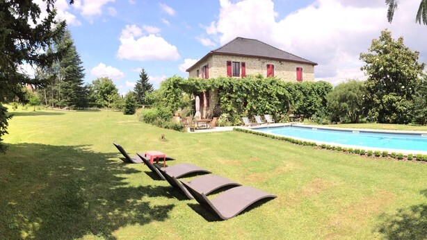Una casa de piedra con piscina, rodeada de césped cuidado y árboles.