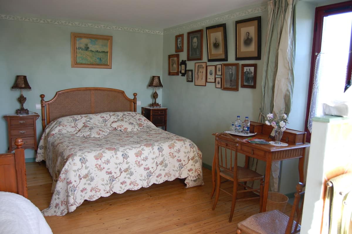 A bedroom with a wooden bed, a desk with a chair, a nightstand, and a wall with framed pictures.