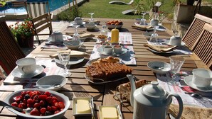 Una mesa de madera lista para el desayuno, con un tazón de fresas, un pastel, mantequilla y una cafetera.