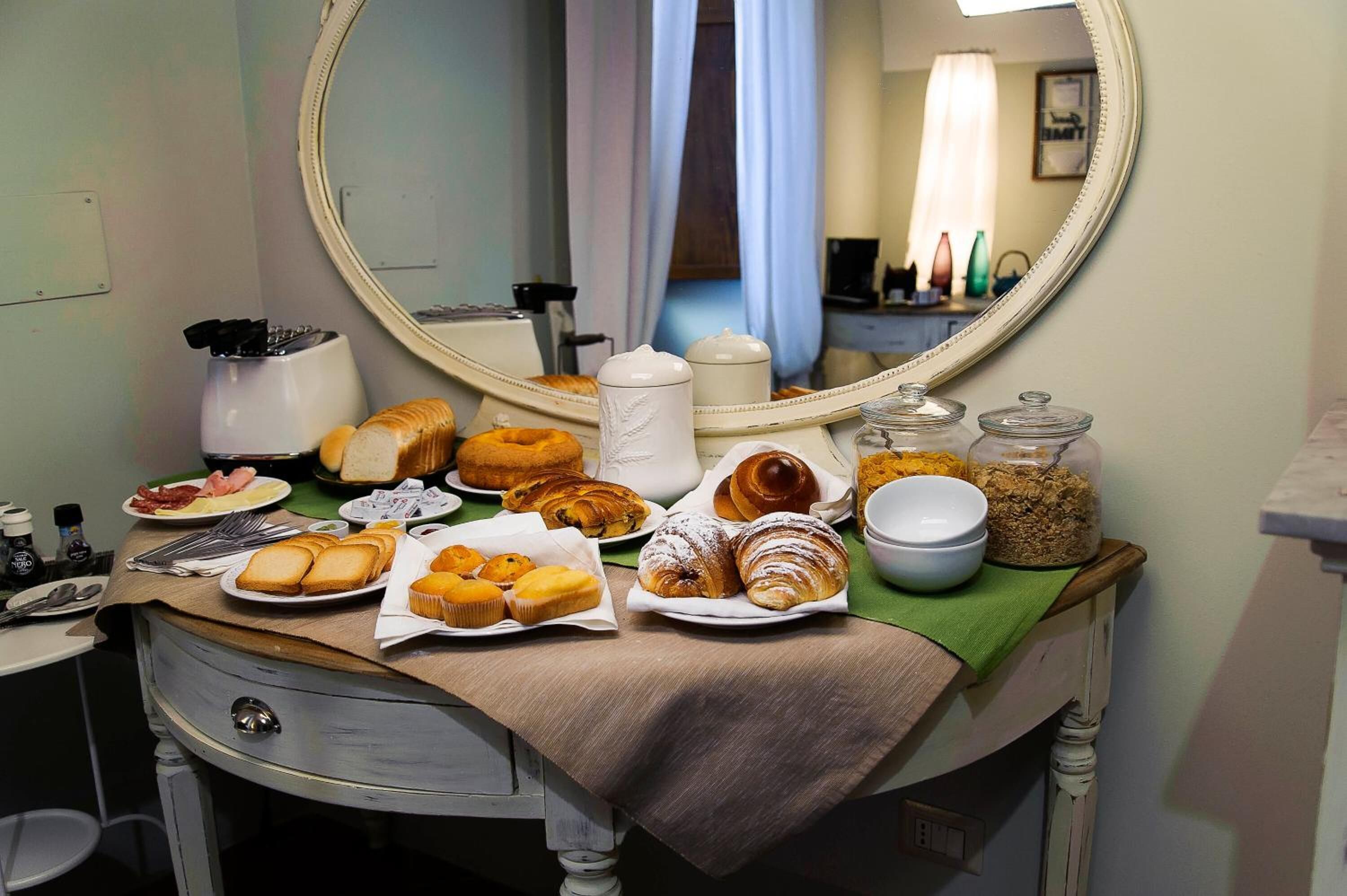 A breakfast buffet with various pastries and bread on a table, a mirror, and a window with curtains.