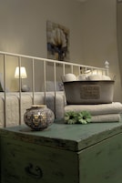 Un dormitorio con estructura de cama metálica, lámpara de noche, un recipiente decorativo de metal con la etiqueta 'FLEURS & FLOWERS' y un aparador verde.