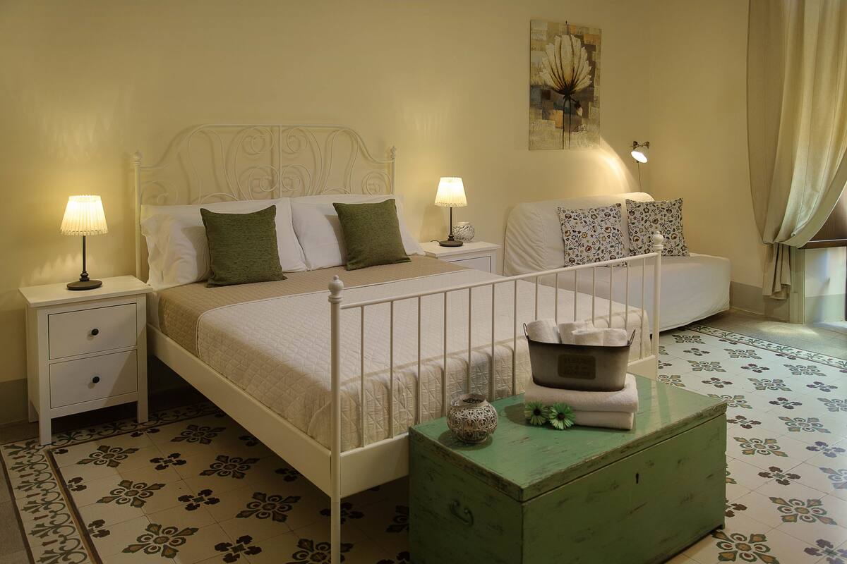 Une chambre à coucher avec un lit, deux tables de chevet, une commode, une commode verte et un sol à motifs.