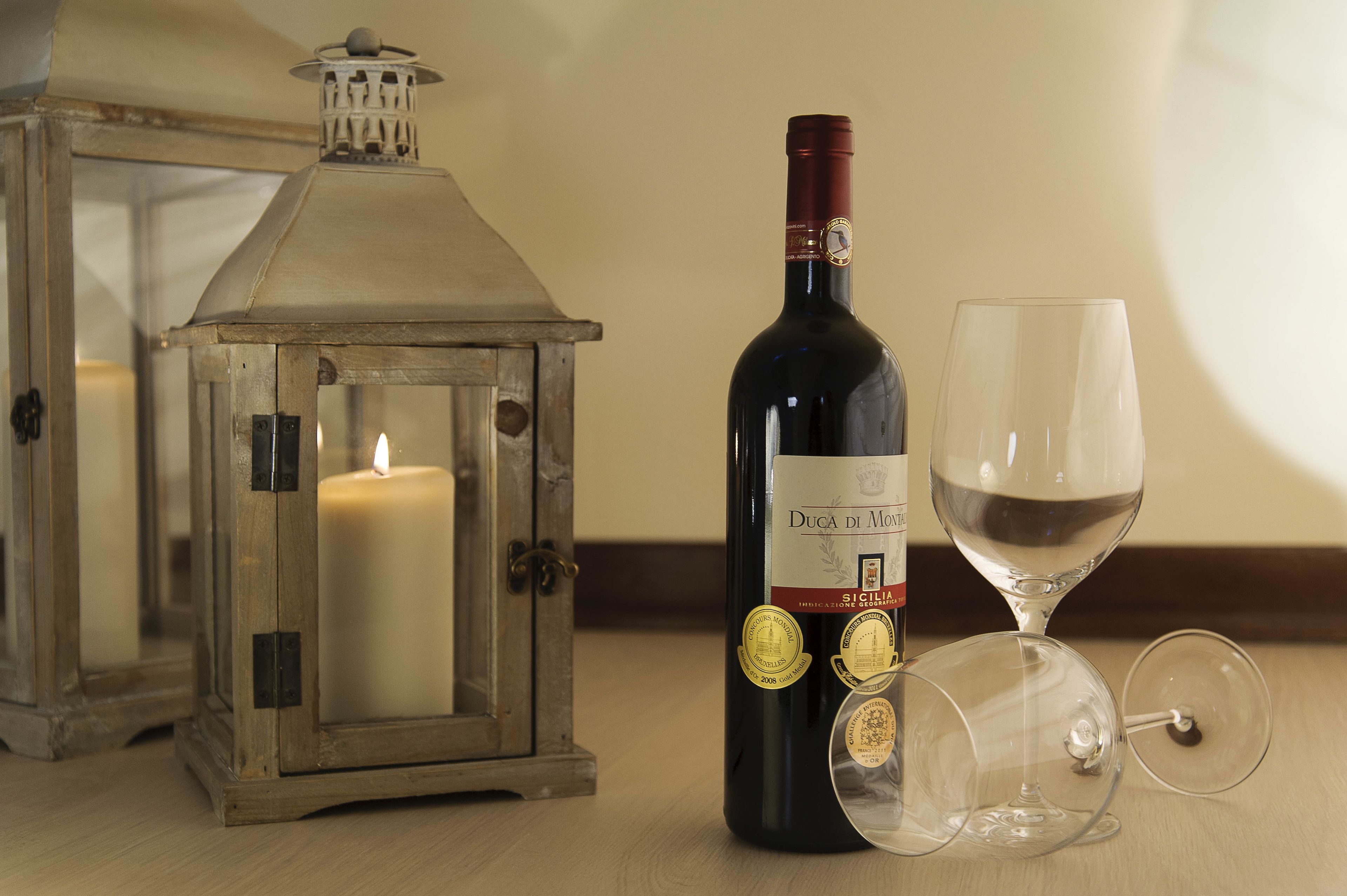 A candle inside a lantern, a bottle of wine, and two wine glasses on a table.