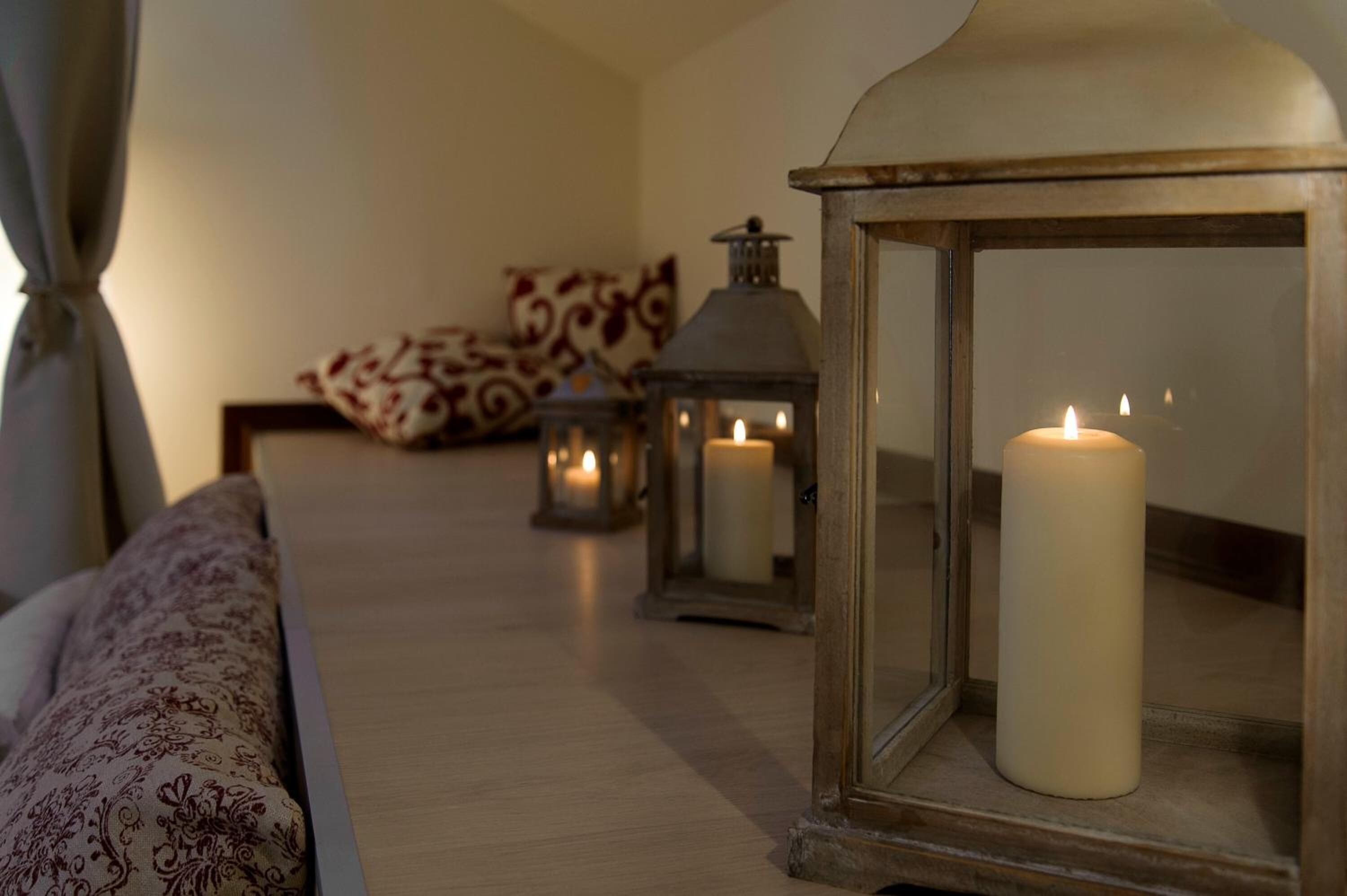 A cozy room with a bed, patterned pillows, and candles in lanterns.