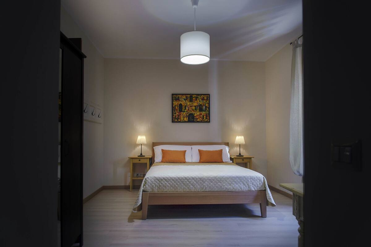 Une chambre à coucher avec un lit, deux lampes de chevet, un luminaire suspendu et un tableau accroché au mur.