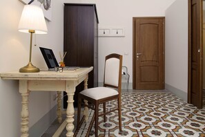 Una stanza con una scrivania in legno, una lampada, una sedia, una porta e un pavimento piastrellato.