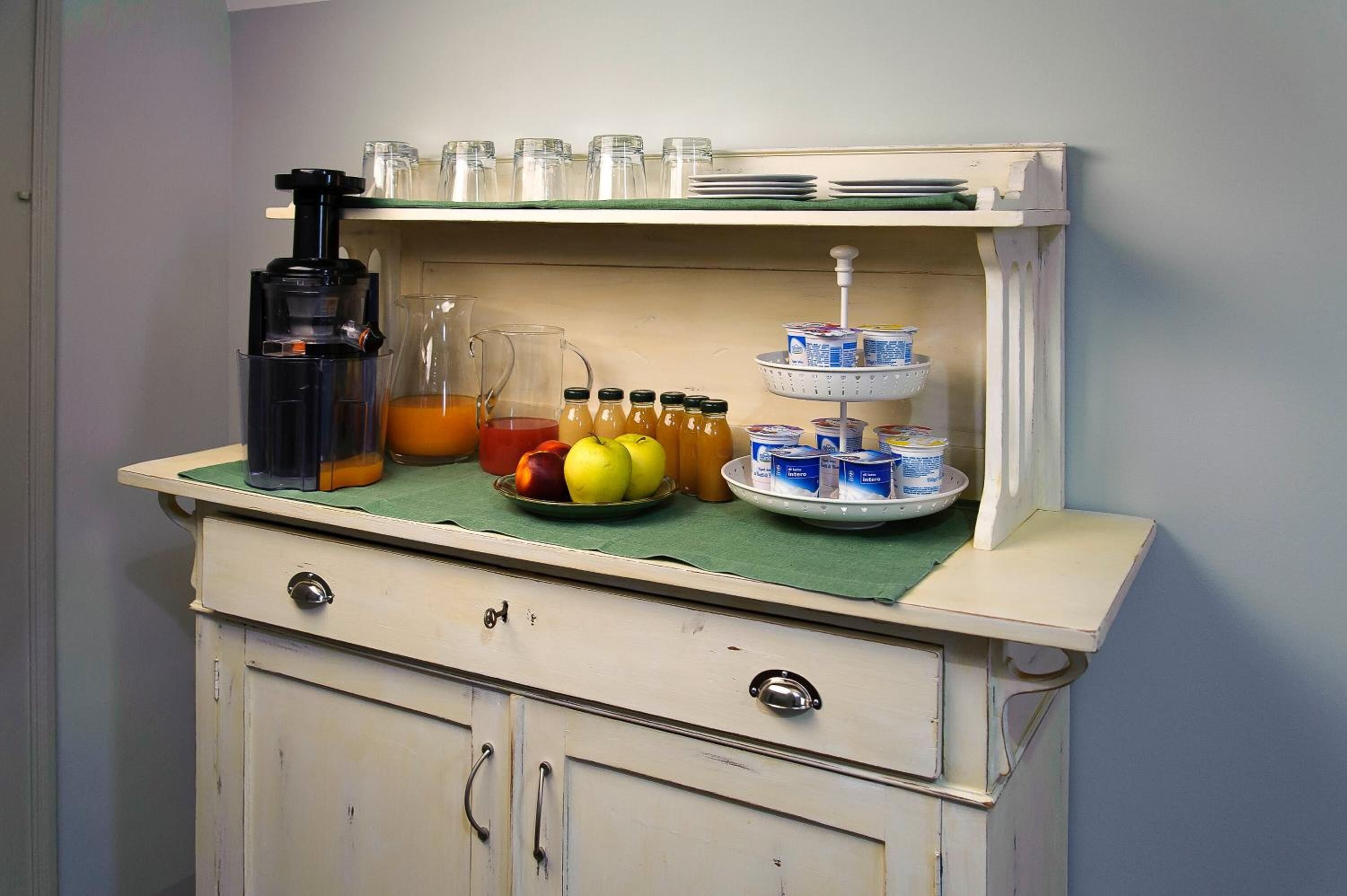 A kitchenette with a coffee maker, fruit bowl, and a three-tiered beverage dispenser.