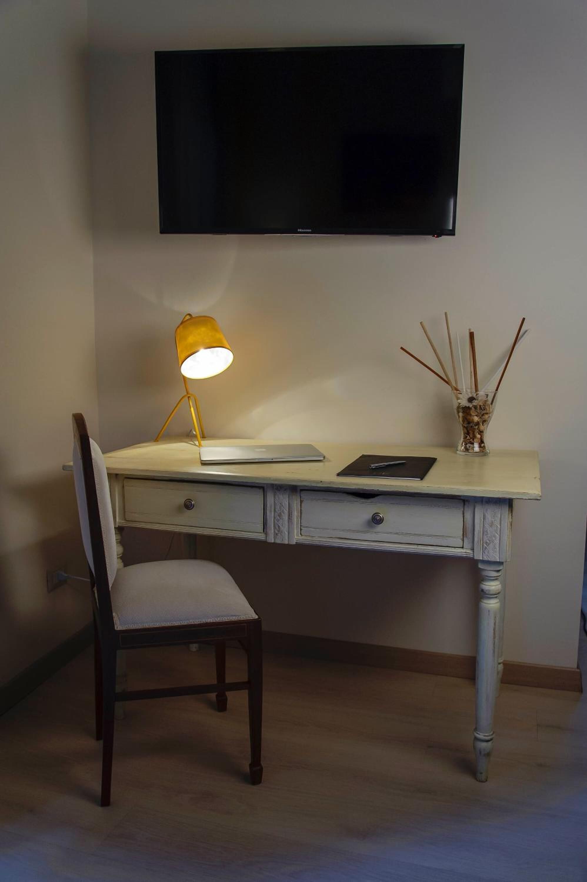 Ein Schreibtisch mit Lampe, ein Stuhl und ein an der Wand befestigter Flachbildfernseher.