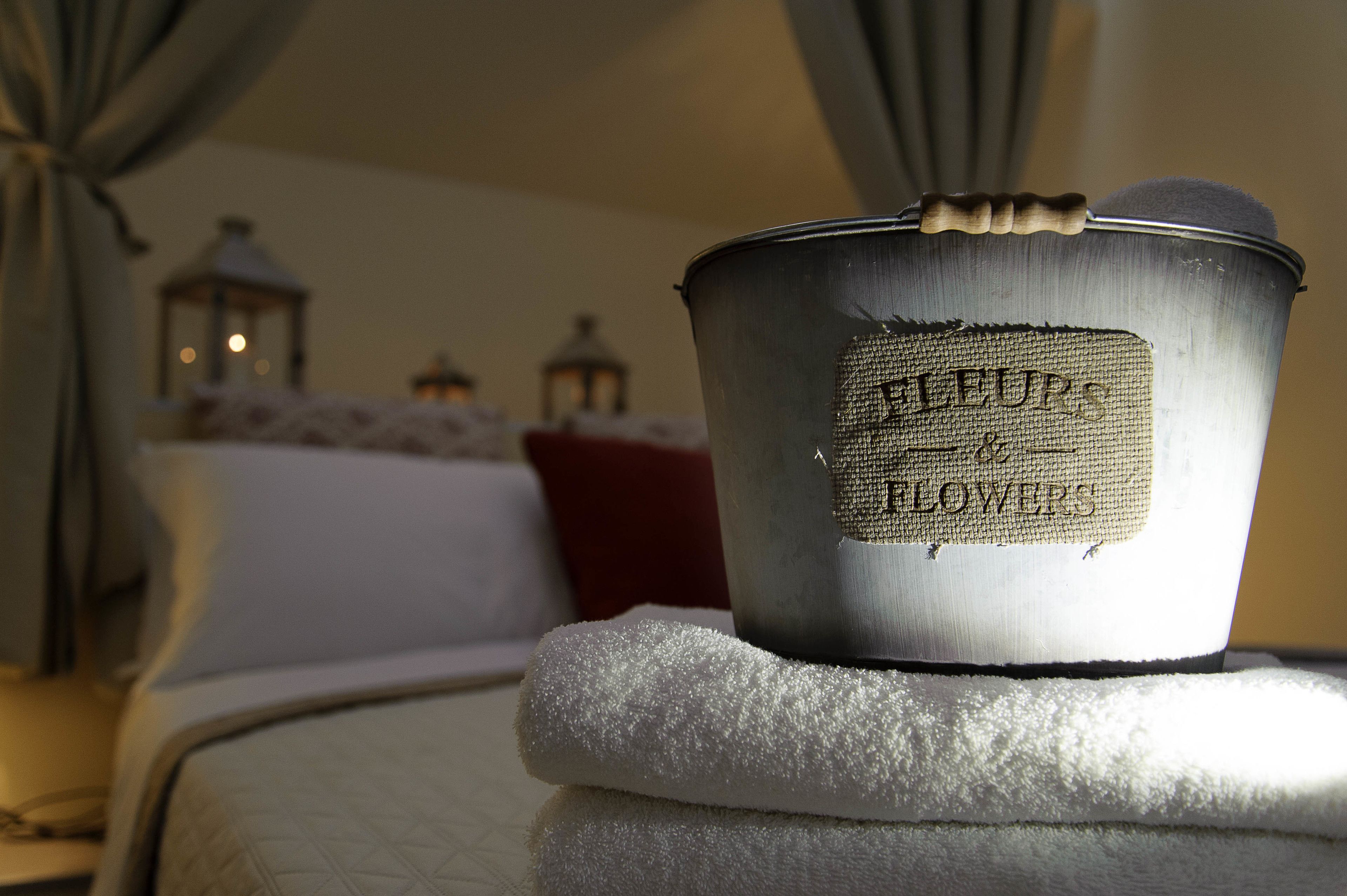 A metal container labeled "FLEURS" on a bed with a white towel.