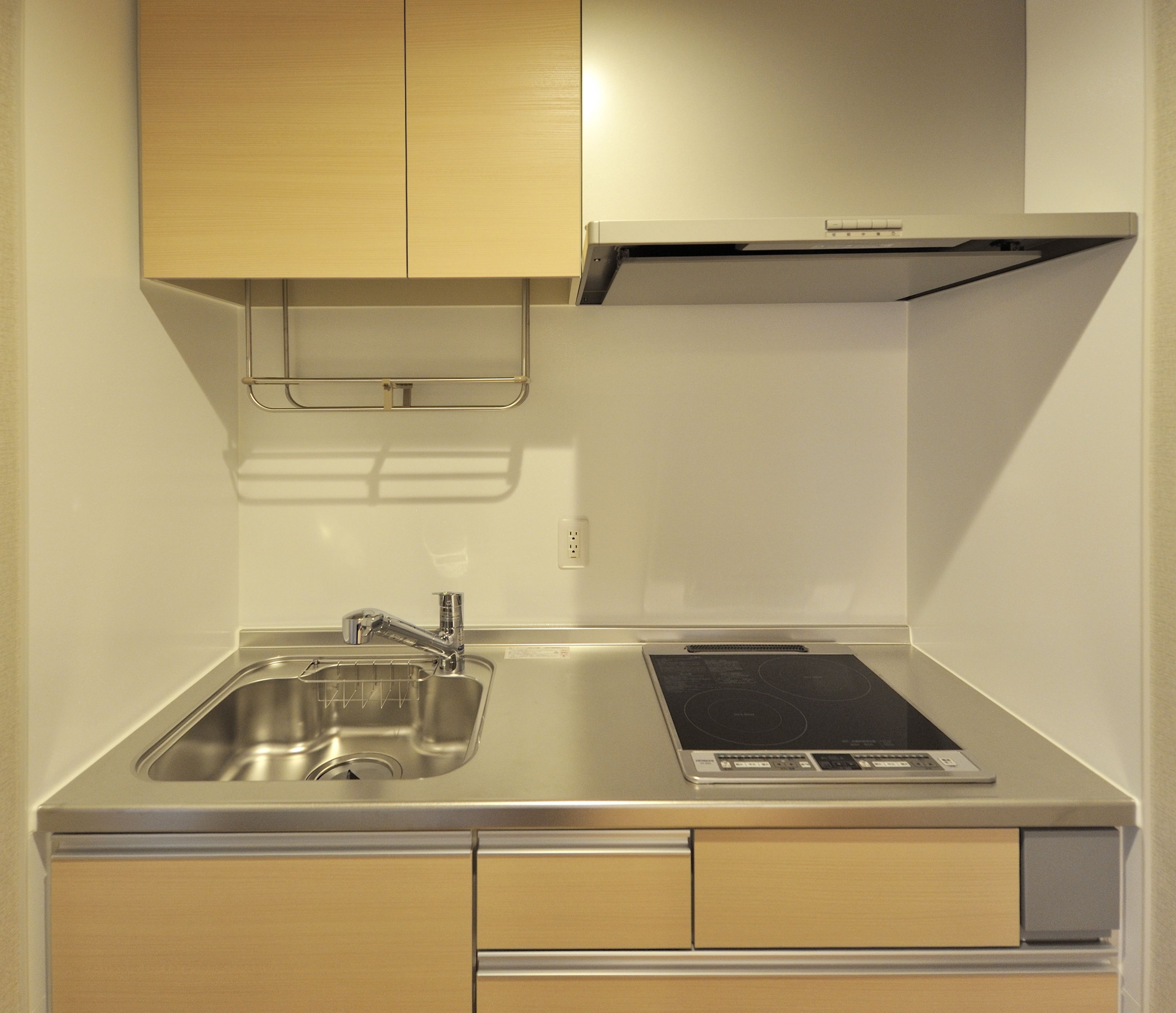 A compact kitchen with a stainless steel sink, a built-in stovetop, and wooden cabinets.