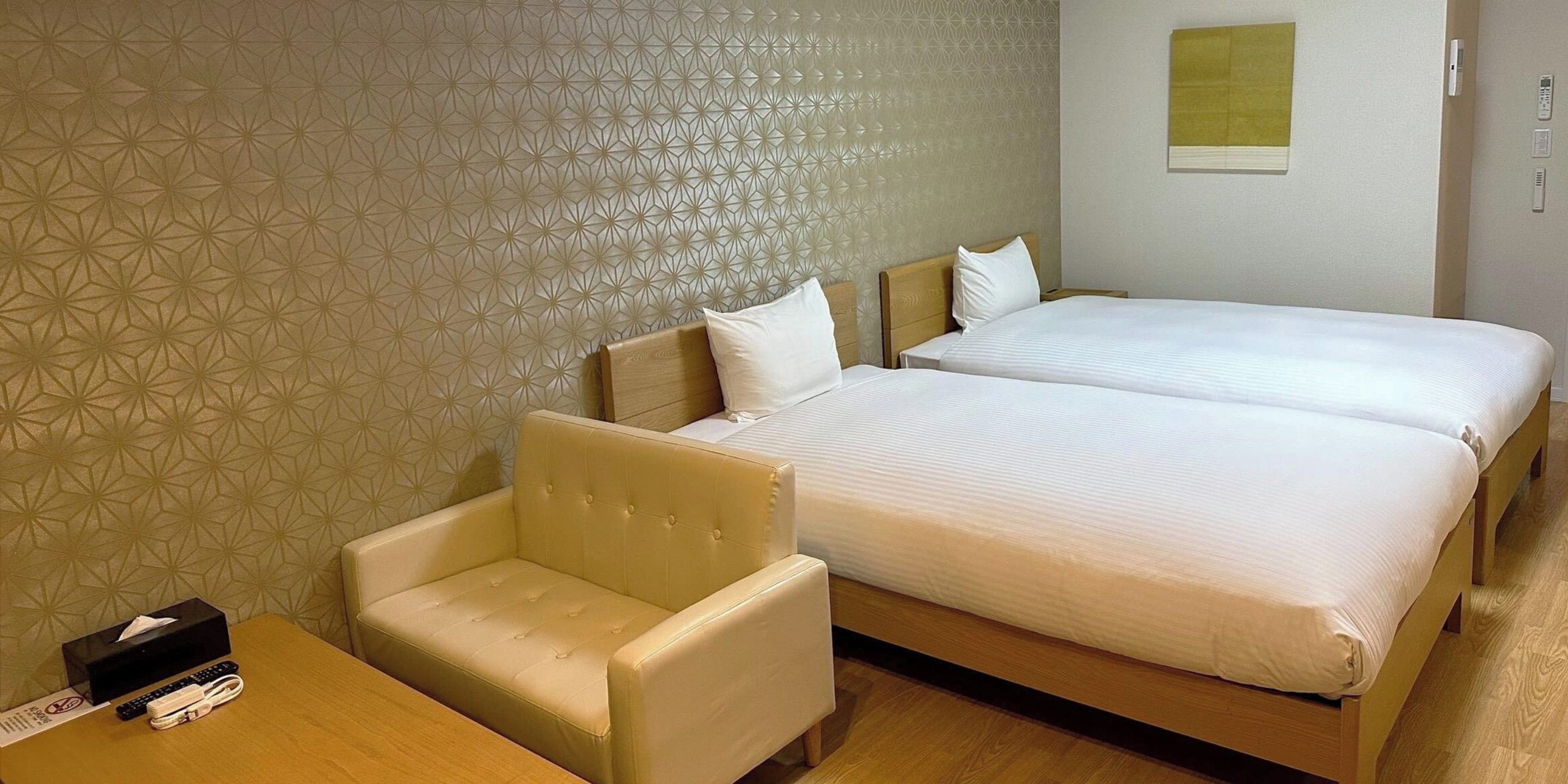 A hotel room with two beds, a sofa, a table, and a patterned wall.