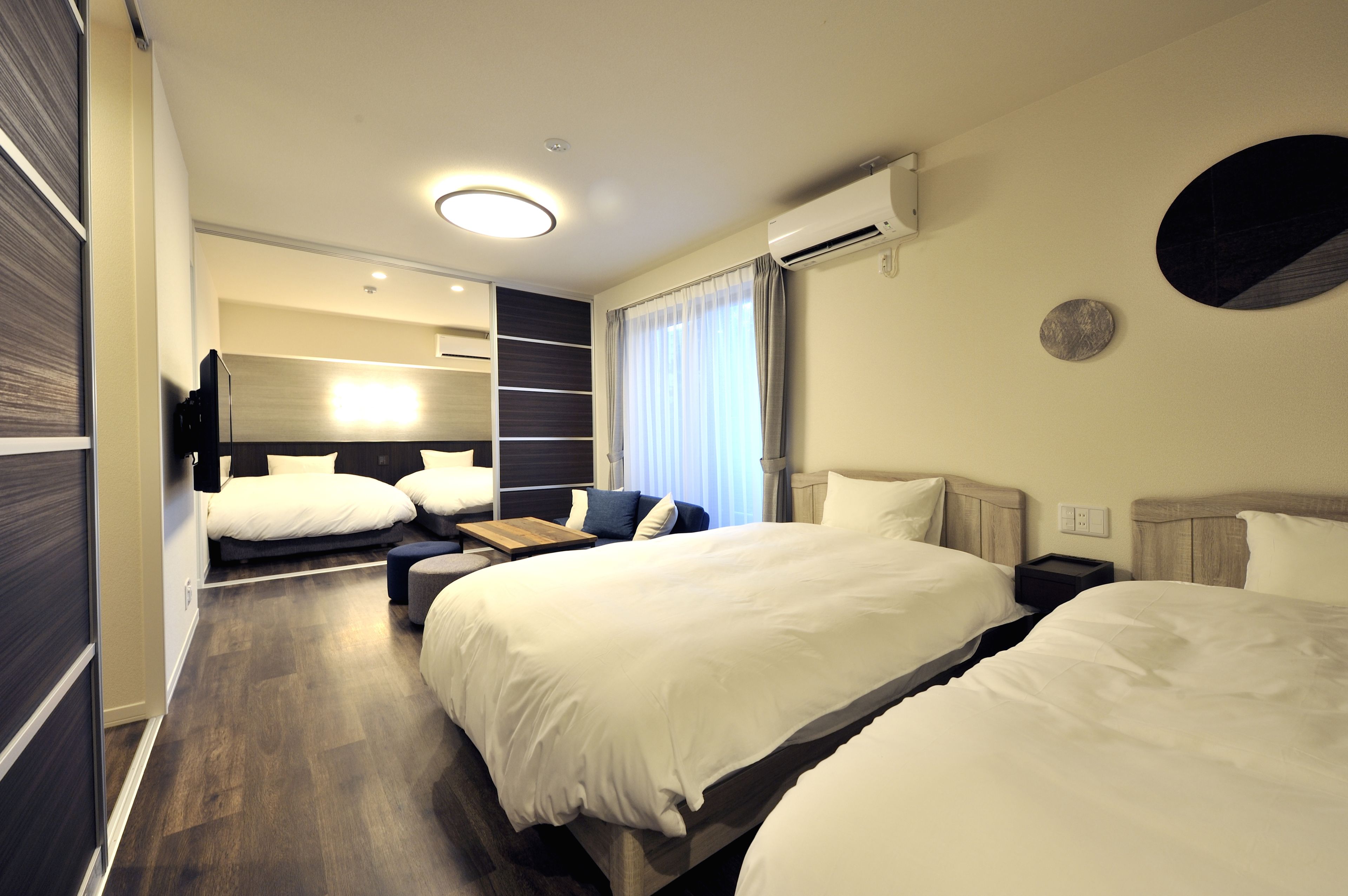 Une chambre d’hôtel avec deux lits, un petit coin salon et une grande fenêtre avec des rideaux.