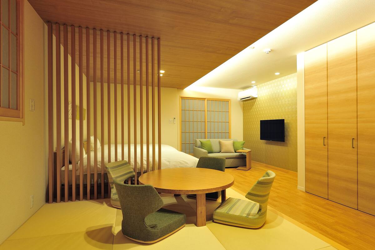 A modern hotel room with a bed, a sofa, a TV, and a wardrobe.