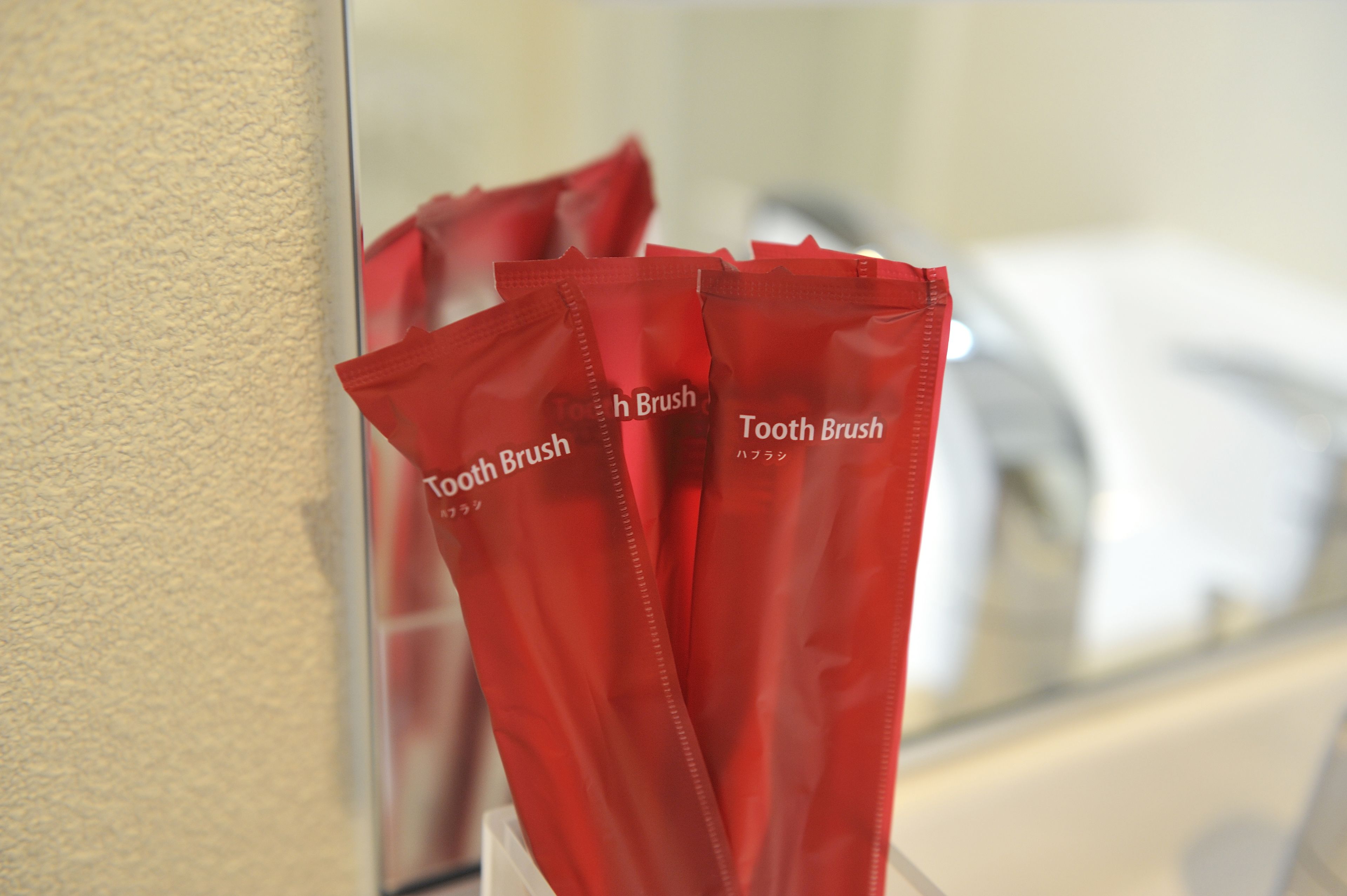 Ein Badezimmer mit Spiegel, der eine Zahnbürste und eine rote Zahnbürstenetui reflektiert.