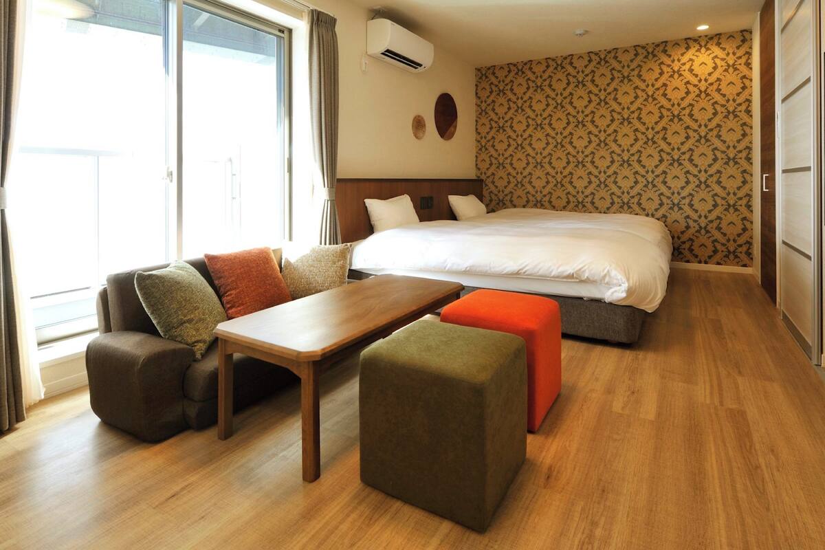 A hotel room with a bed, a sofa, a table, and a small ottoman.