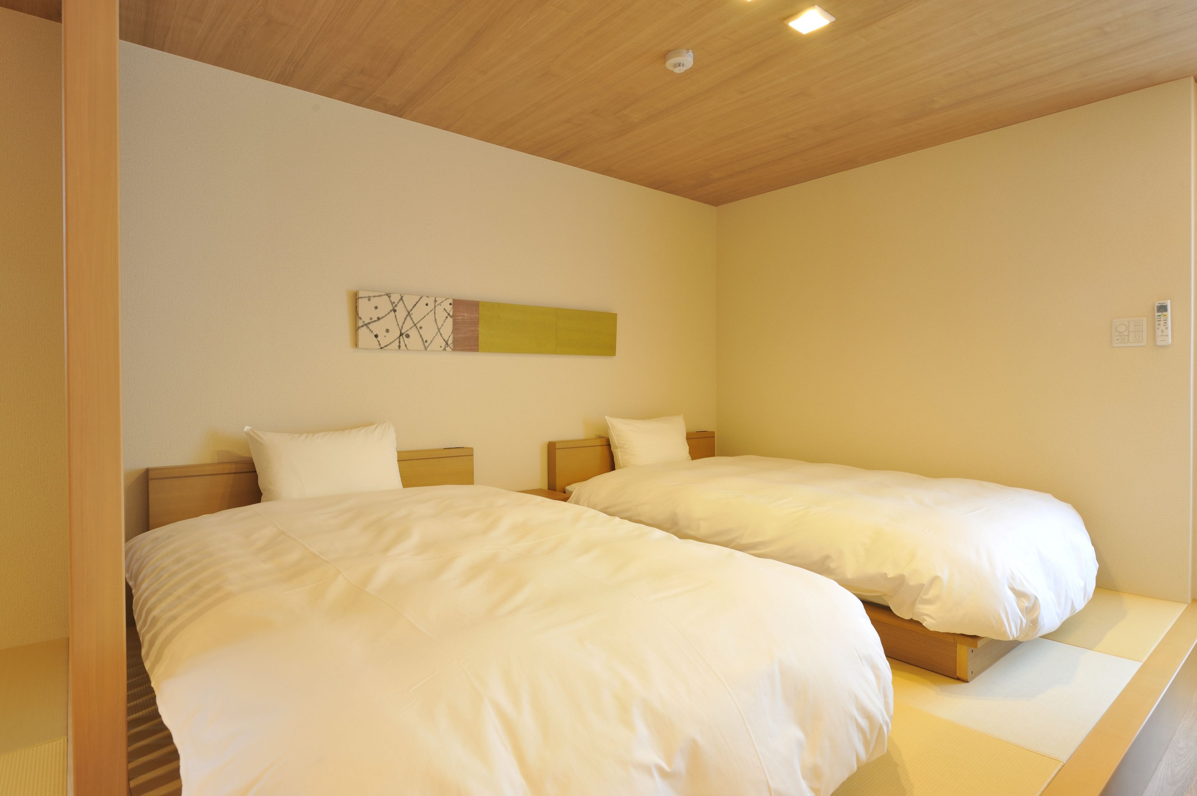 Une chambre d’hôtel avec deux lits simples, des têtes de lit en bois, un petit tableau décoratif au mur et un luminaire au plafond.