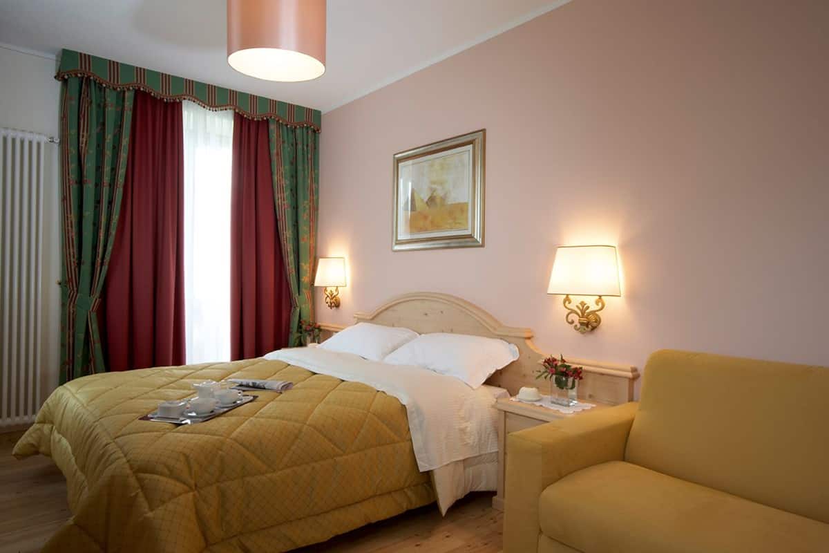 Habitación de hotel con cama, dos lámparas de noche, mesita de noche, una silla y un cuadro en la pared.