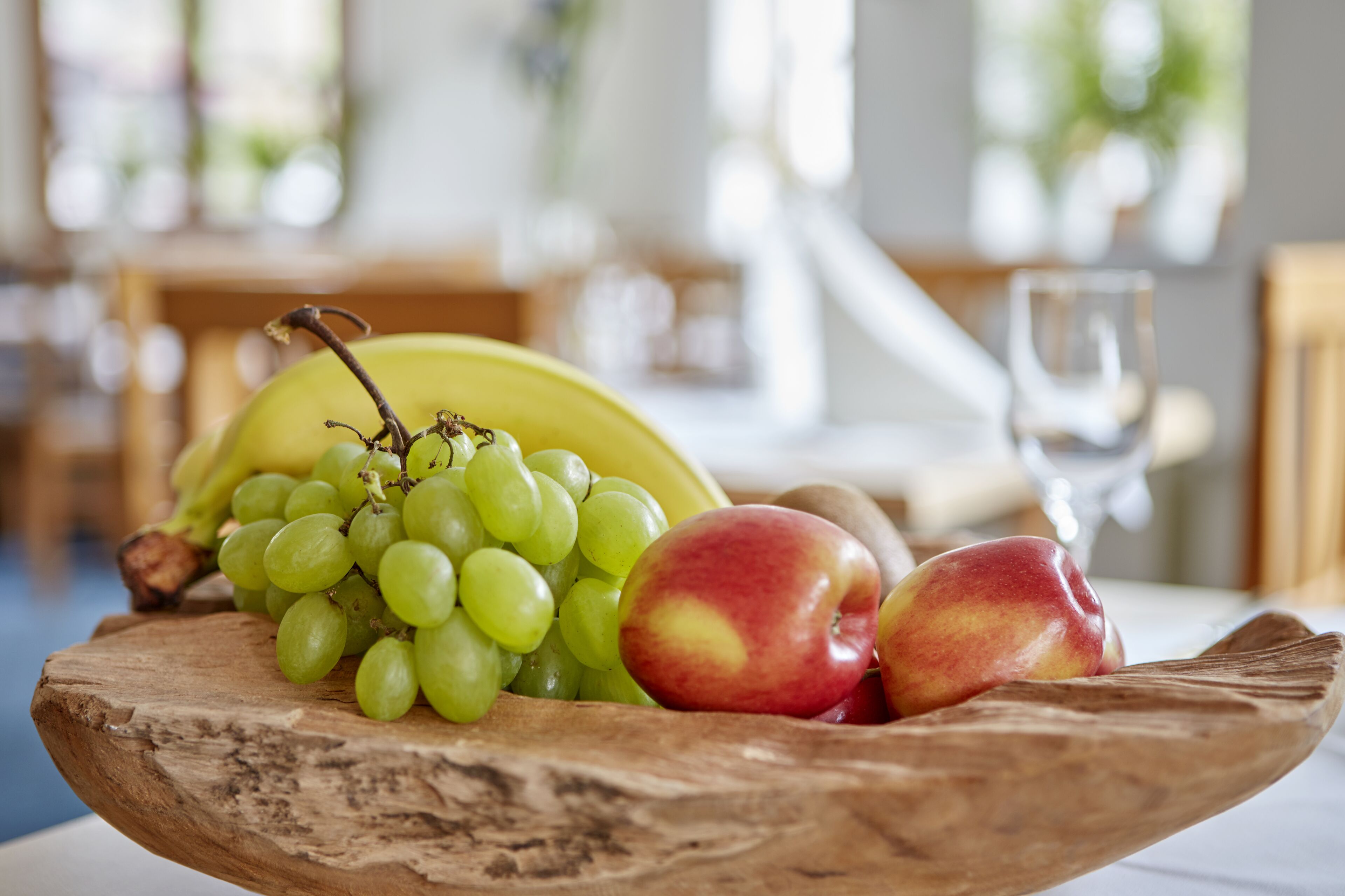 Un cuenco de madera con uvas verdes, manzanas rojas y amarillas, y un plátano sobre una mesa.