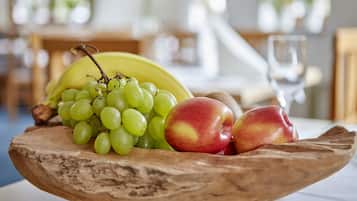 Un cuenco de madera con uvas verdes, manzanas rojas y amarillas, y un plátano sobre una mesa.
