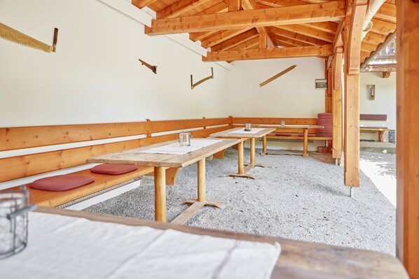 An indoor wooden cabin with benches and tables, a saw blade on the wall, and a gravel floor. - Alte Säge Ruhpolding (Ruhpolding)