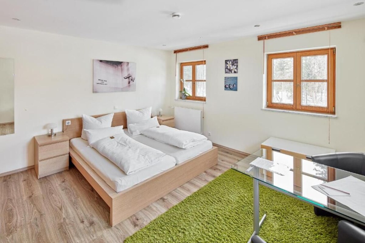 A modern bedroom with a bed, bedside tables, a desk, and a green rug.