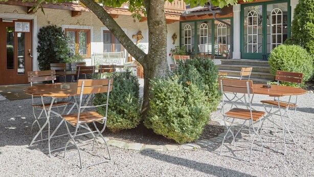 An outdoor seating area with tables and chairs, surrounded by gravel, under a tree. - Alte Säge Ruhpolding (Ruhpolding)