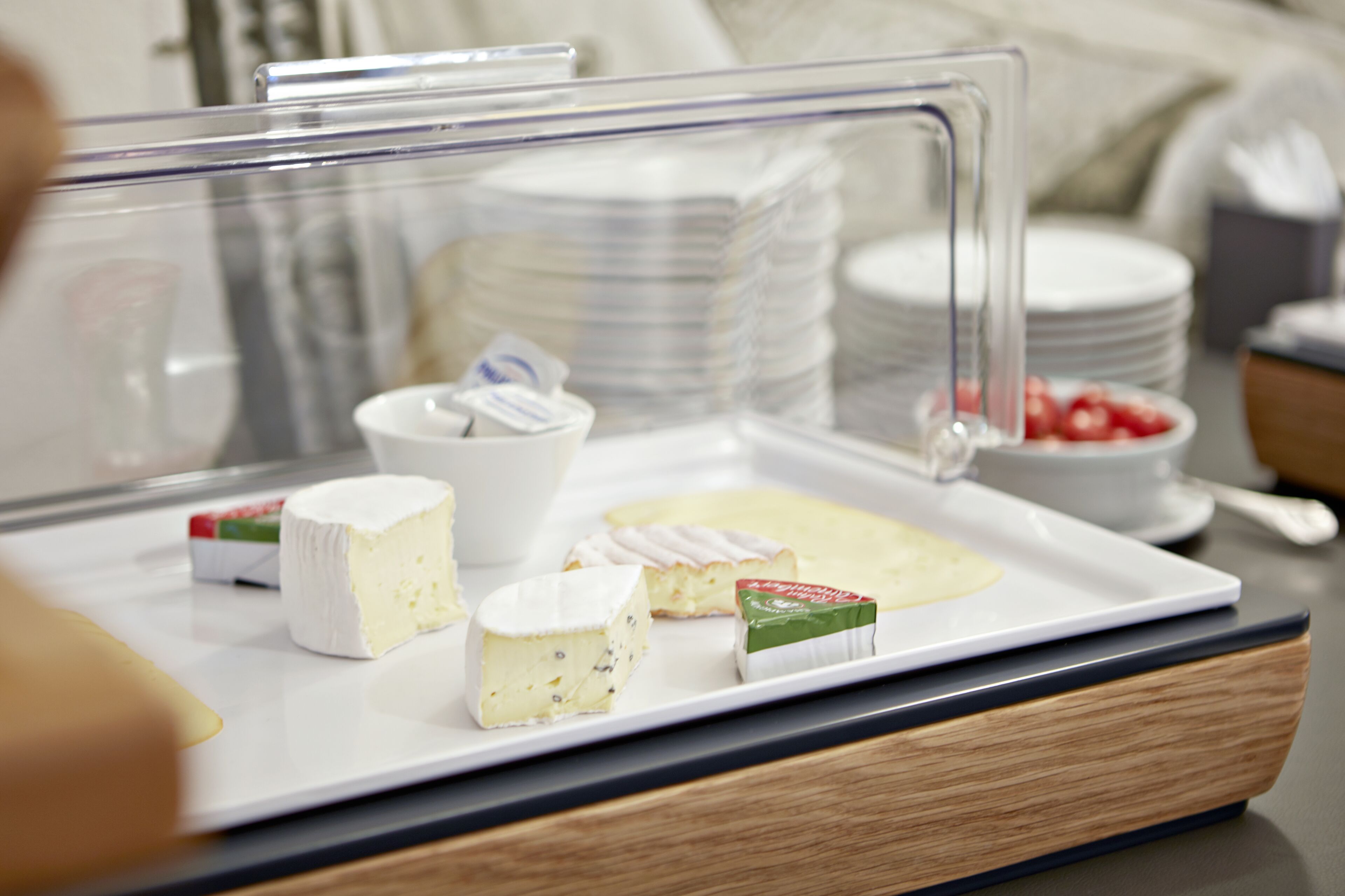 A cheese display with various types of cheese and a small bowl of strawberries.