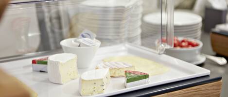 A cheese display with various types of cheese and a small bowl of strawberries.