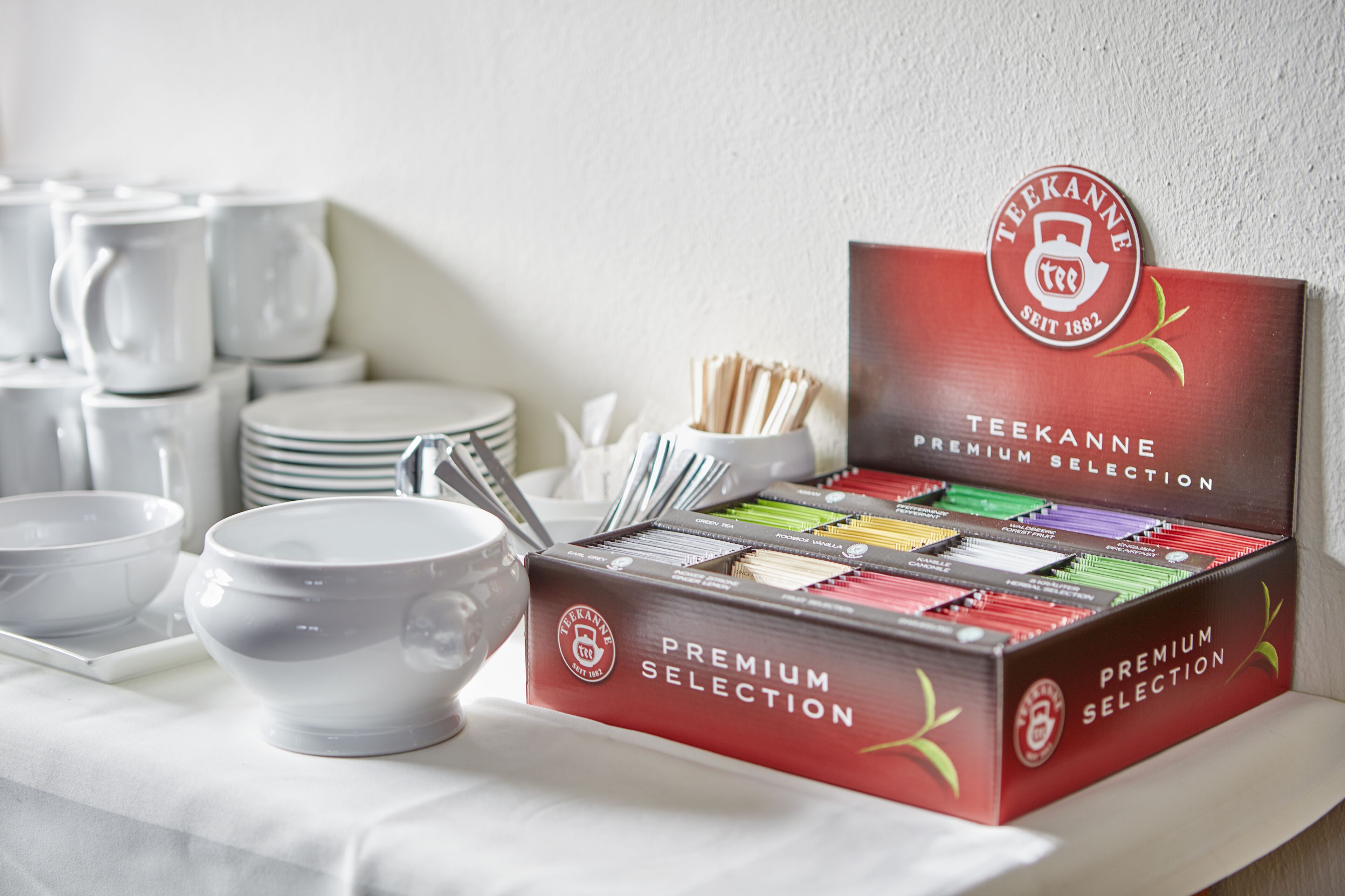 A Teekanne premium selection box on a table with white bowls and cups.