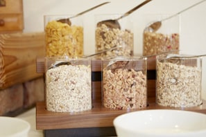 Four glass containers with different types of granola on a wooden tray.