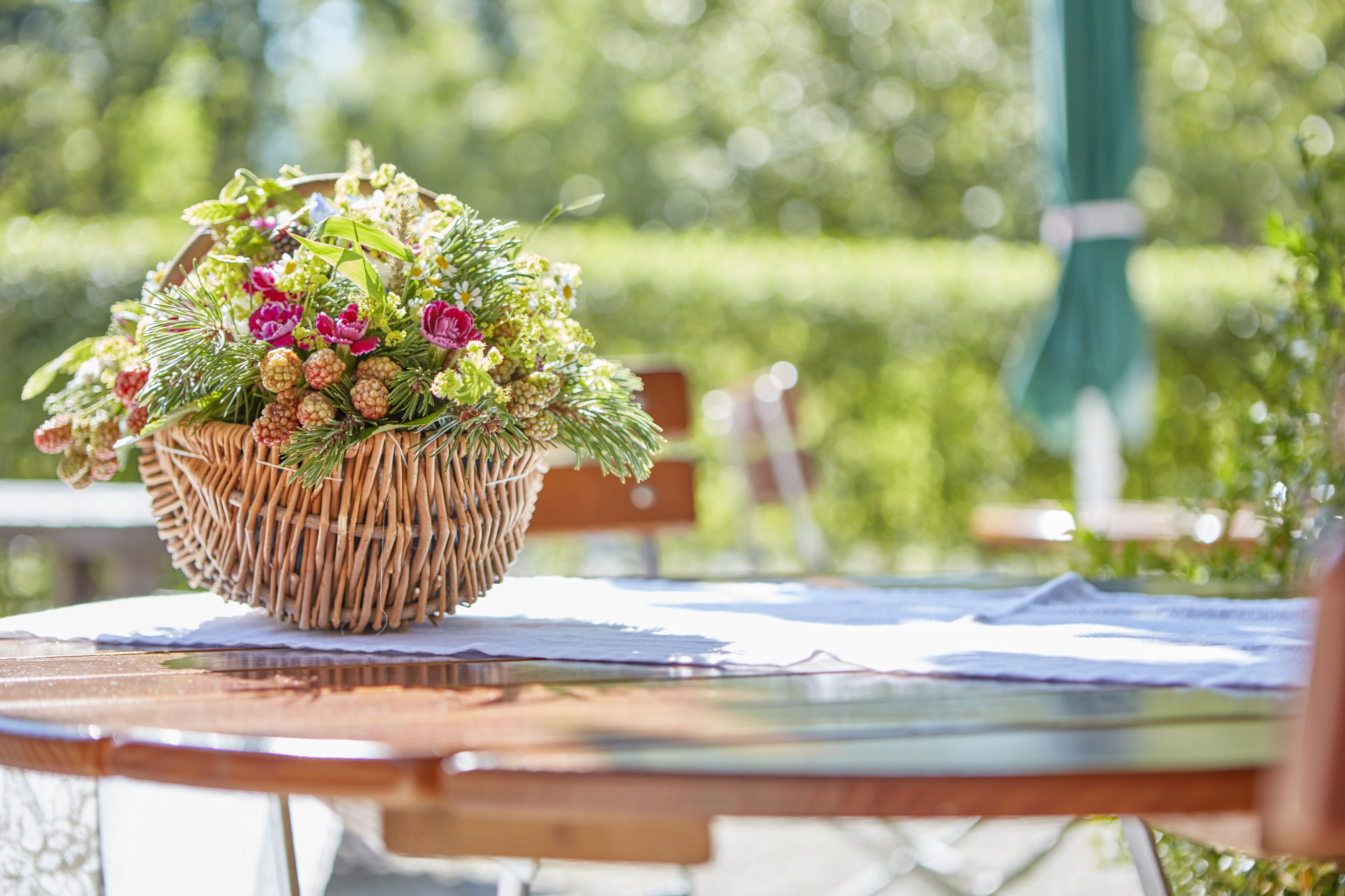 Un cesto di vimini colmo di fiori e piante verdi su un tavolo all'aperto.