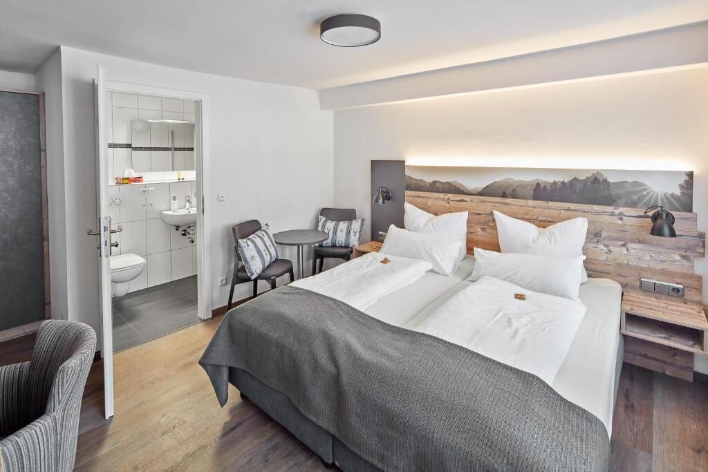 A modern hotel room with a large bed, a small desk, a chair, a bathroom, and a scenic wall mural.