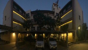 A multi-story hotel with a central courtyard, two cars parked in front, and a well-lit entrance. - Hotel Orange Inn (Ahmedabad)