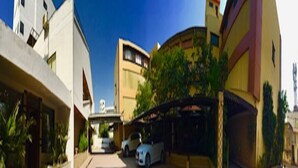 A modern building with a curved facade, a covered parking area, and a white car parked in front. - Hotel Orange Inn (Ahmedabad)