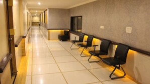 A hotel corridor with a long reception desk, several black chairs, and a tiled floor. - Hotel Orange Inn (Ahmedabad)