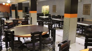 A spacious dining area with multiple tables and chairs, a central round table, and a modern design with grey and orange accents. - Hotel Orange Inn (Ahmedabad)