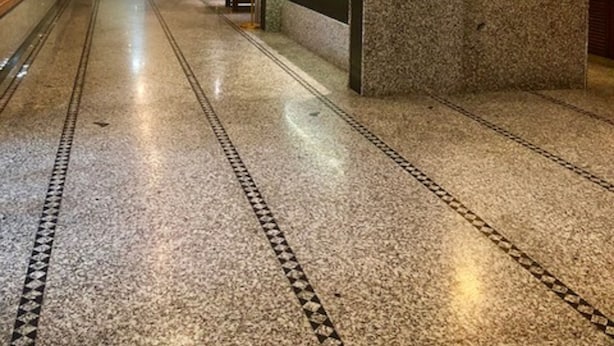 A hotel reception area with a marble floor, a reception desk, and a man standing behind it. - Hotel Orange Inn (Ahmedabad)