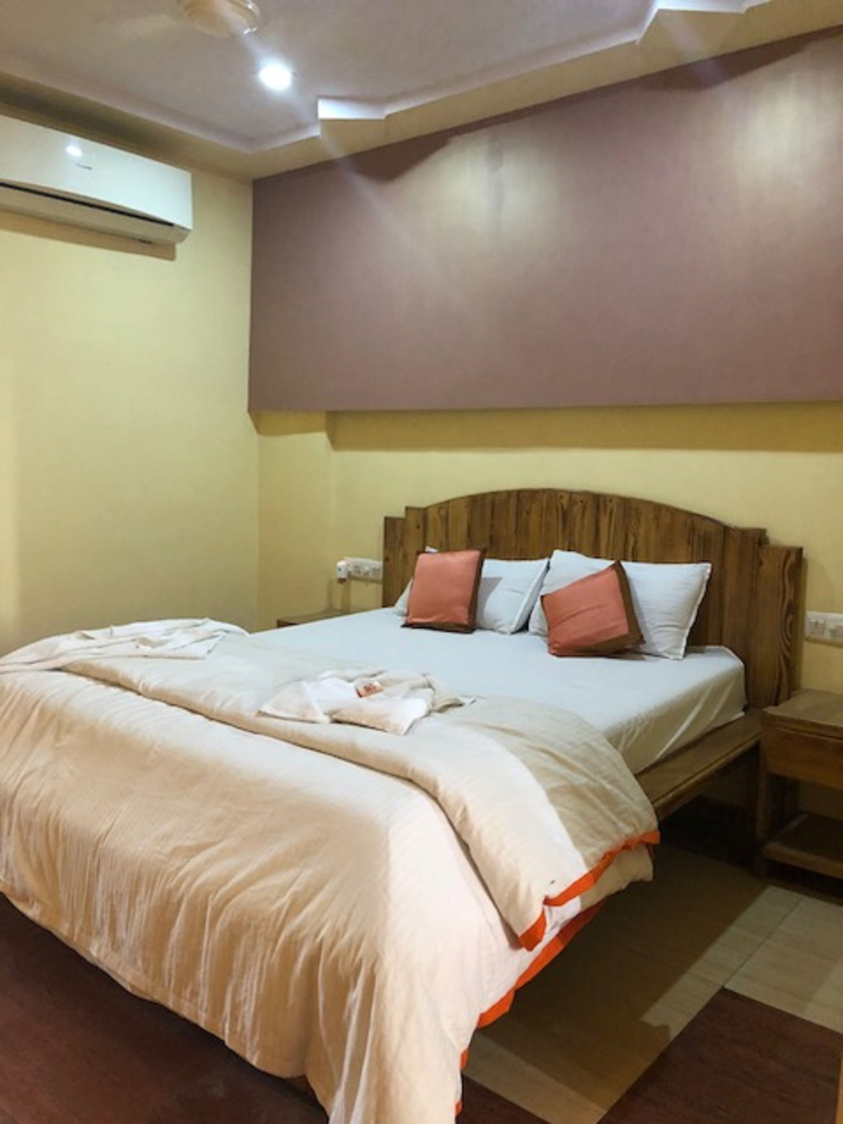 A neatly made bed with a wooden headboard, a bedside table, and an air conditioning unit on the wall.
