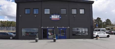 Un edificio moderno con un letrero que dice 'MABY PARKING & HOTEL' y un estacionamiento con varios coches.