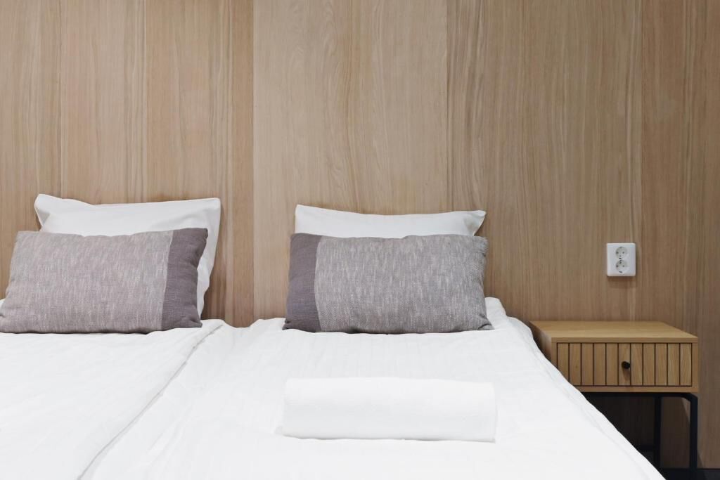 Ett hotellrum med en väggpanel av trä, en säng med vita sängkläder och två kuddar samt ett litet träbord vid sängen med en låda.