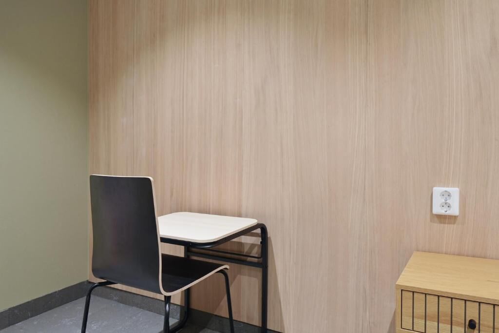 A room with a wooden wall, a black chair with a white seat, and a wooden cabinet.