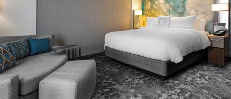 A modern hotel room with a large bed, a sofa, a small table, and a wall with a colorful abstract design.