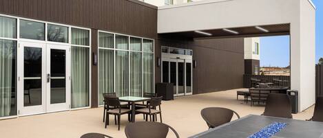An outdoor patio area with a table and chairs, a seating area with a sofa, and a building with large windows and a door.
