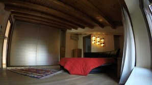Una camera da letto con un letto, una coperta rossa, un soffitto in legno e un'ampia finestra.
