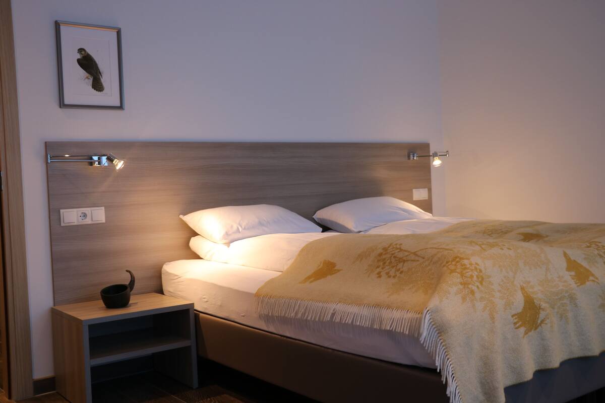 A neatly made bed with a headboard, a bedside table with a cup, and a framed picture on the wall.