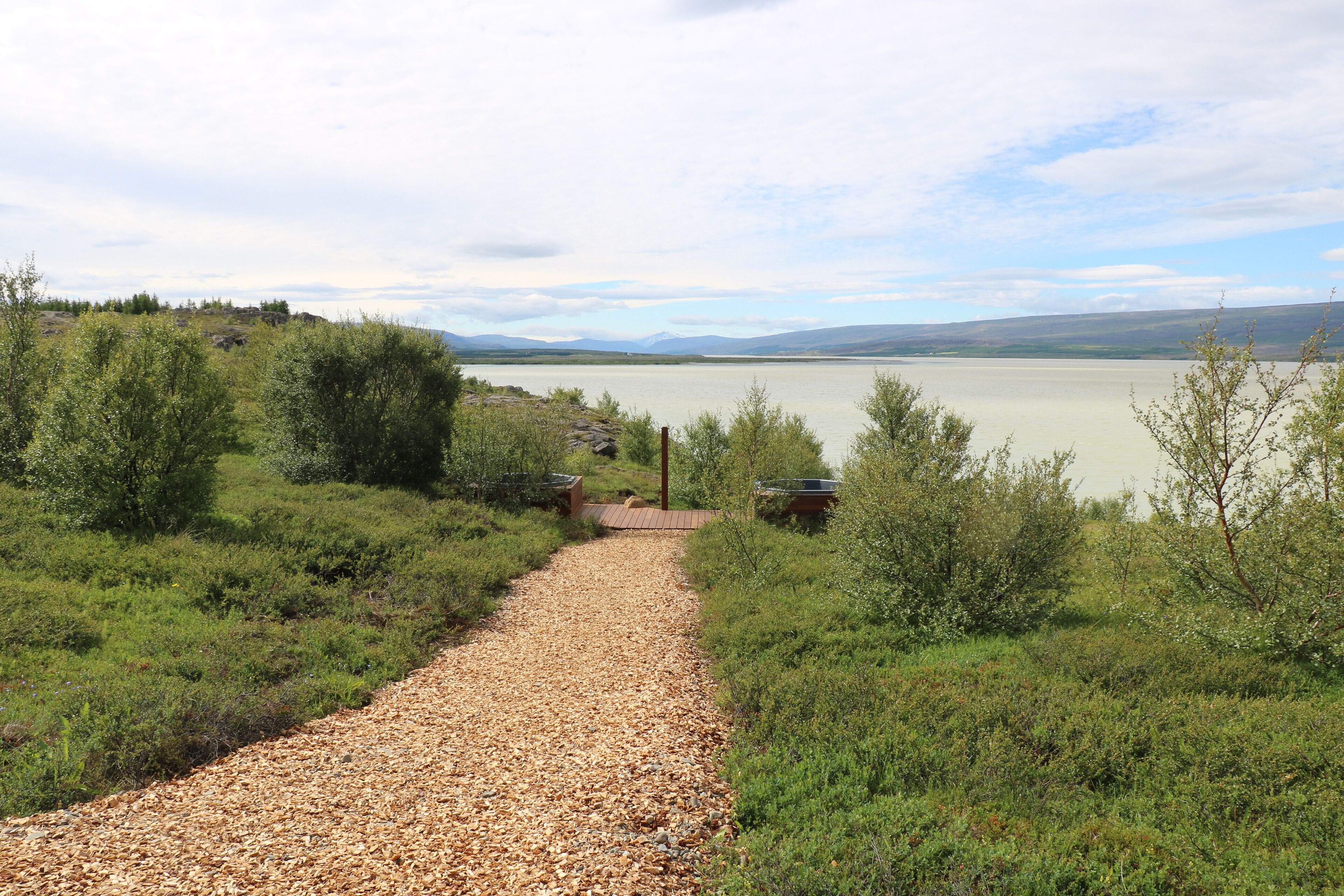 A gravel path leading to a body of water with a view of distant mountains.