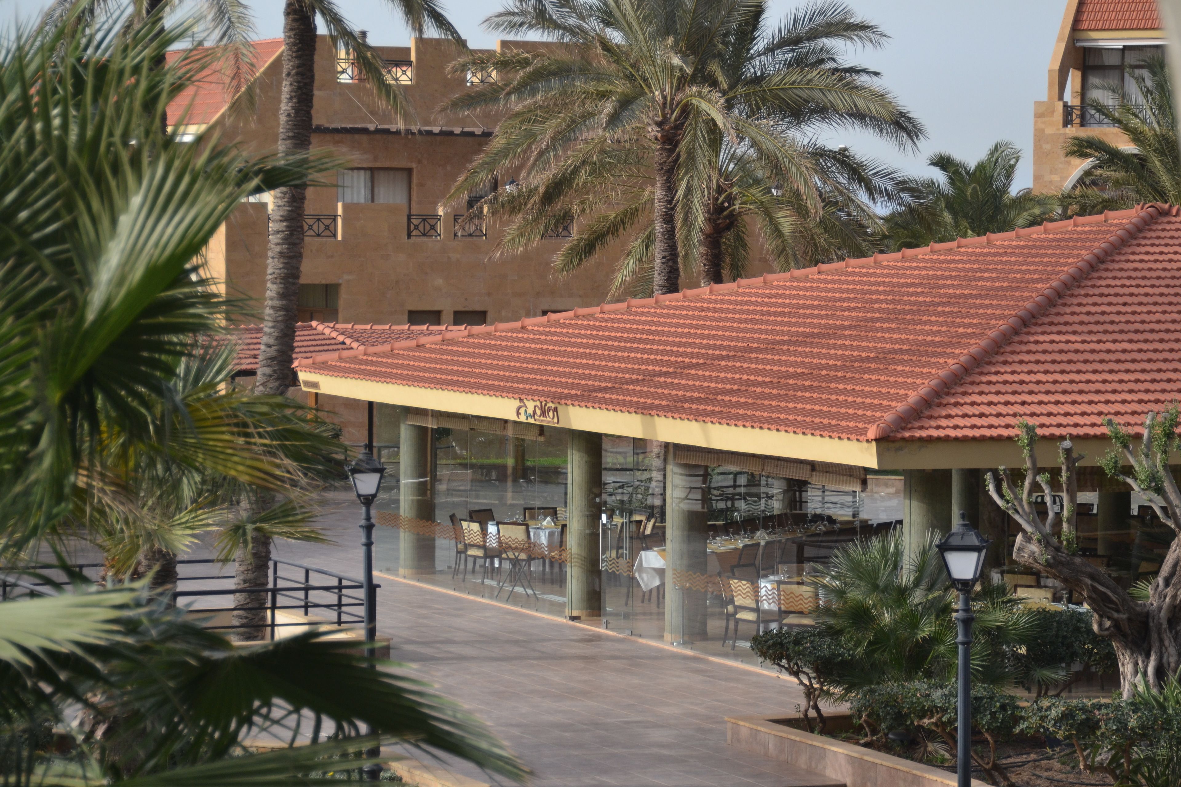 A building with a red-tiled roof, palm trees, and outdoor seating areas.