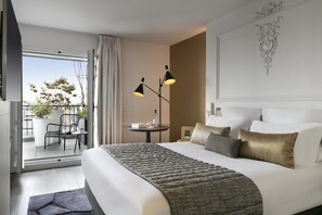 A hotel room with a large bed, a view of the outdoors, a small table with a lamp, and a balcony with chairs and a potted plant. - La Clef Champs-Élysées Paris by The Crest Collection (Paris)