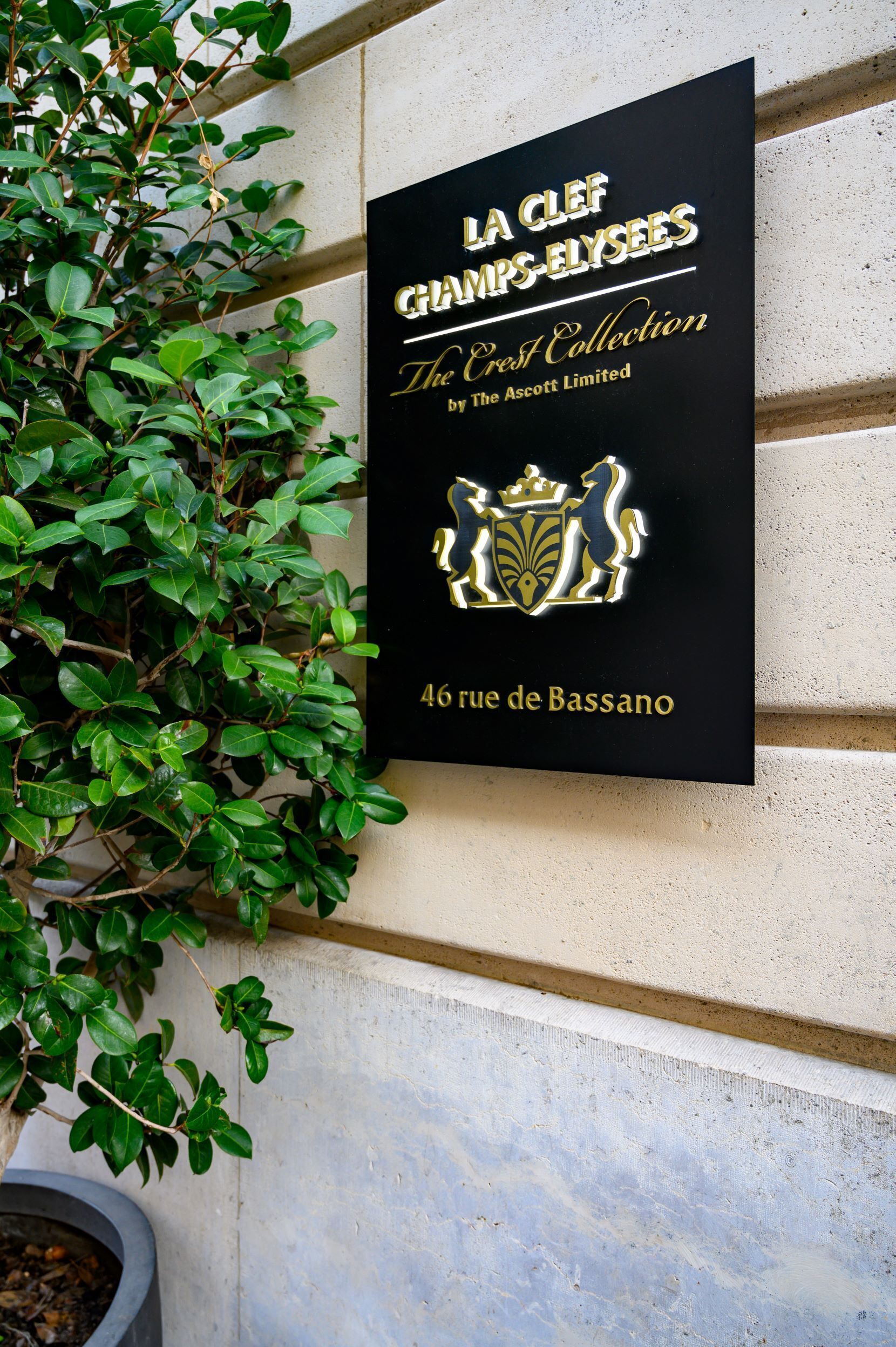 A black sign with gold lettering for 'La Clez Champs-Elysees The East Collection by The Ascott Limited' and an address '46 rue de Bassano'.