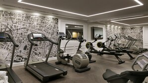 Une salle de sport équipée de tapis de course, de vélos elliptiques et d’un mur recouvert de miroirs.
